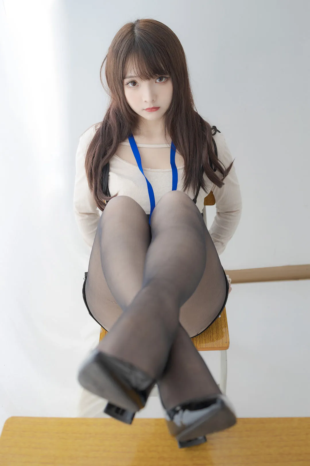 古川kagura坐在椅子上，白色上衣搭配蓝色挂带，深色薄袜前景靠近镜头，背景简洁明亮。