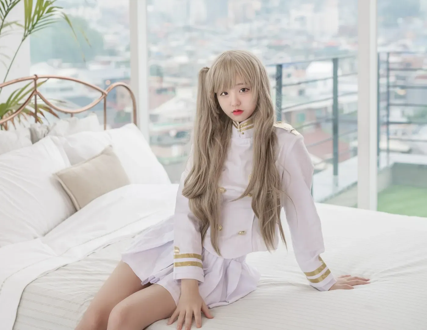 JeongJenny(정제니)浅金长发穿白色制服坐在床边,身后是落地窗和城市背景