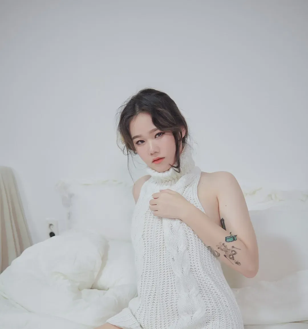 Sira(시라)盘发穿白色针织无袖上衣，坐在浅色床铺前看向镜头