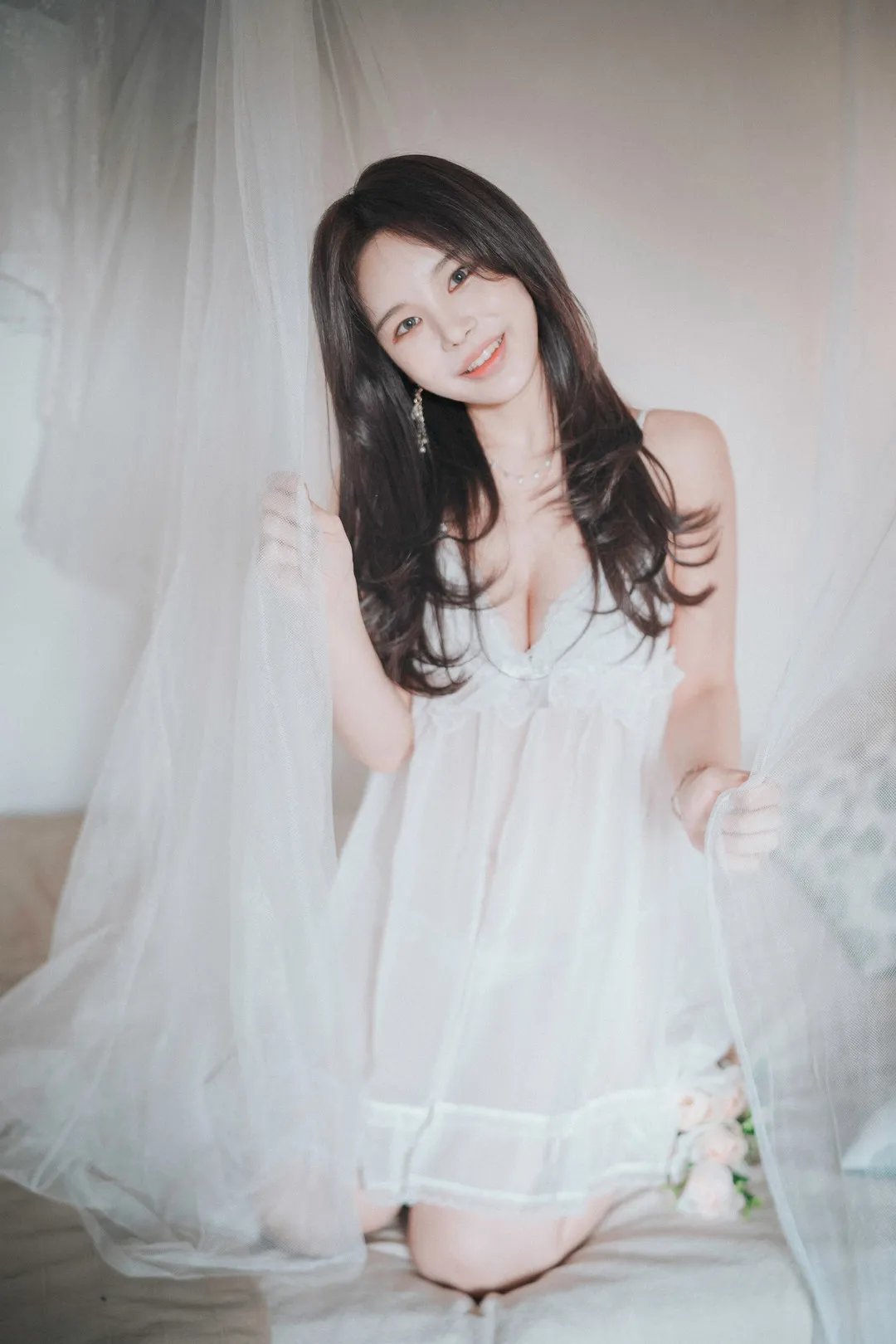 Zzyuri(쮸리)深色长发、白色吊带裙、手扶白色薄纱,跪坐在浅色室内床面的照片