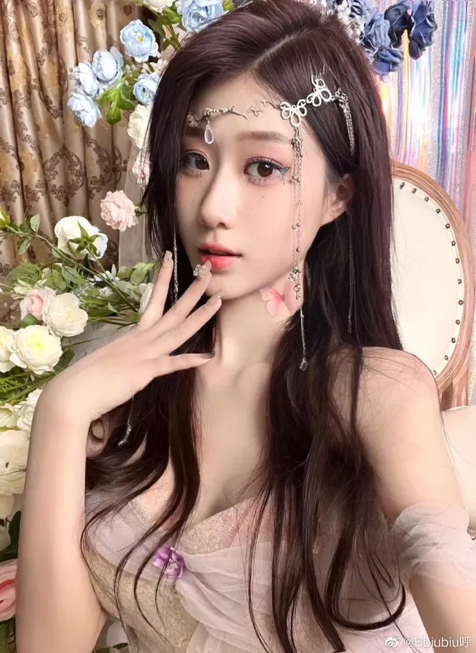 bbiubiu呼长发戴银色额饰,穿浅粉色服饰,身后有花束和椅背