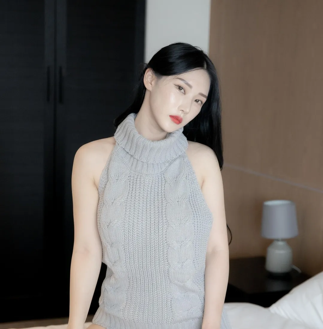 Riha(리하)黑色长发灰色针织上衣造型,坐在室内床边,背景有床头柜和台灯