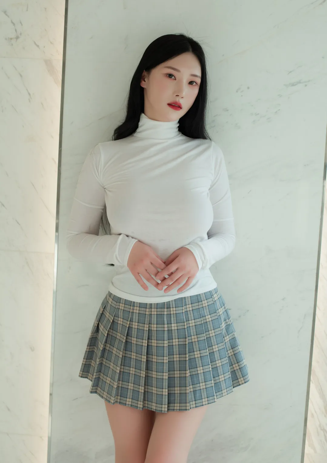 Riha(리하)黑色长发白色高领上衣和格纹裙站姿，背景为浅色石材墙面