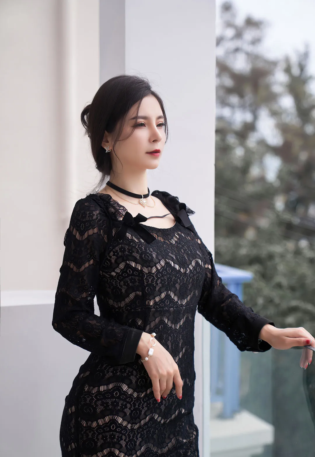 小蛮妖Yummy黑色蕾丝服装照片，人物靠近白色墙面，后方为虚化户外景色。