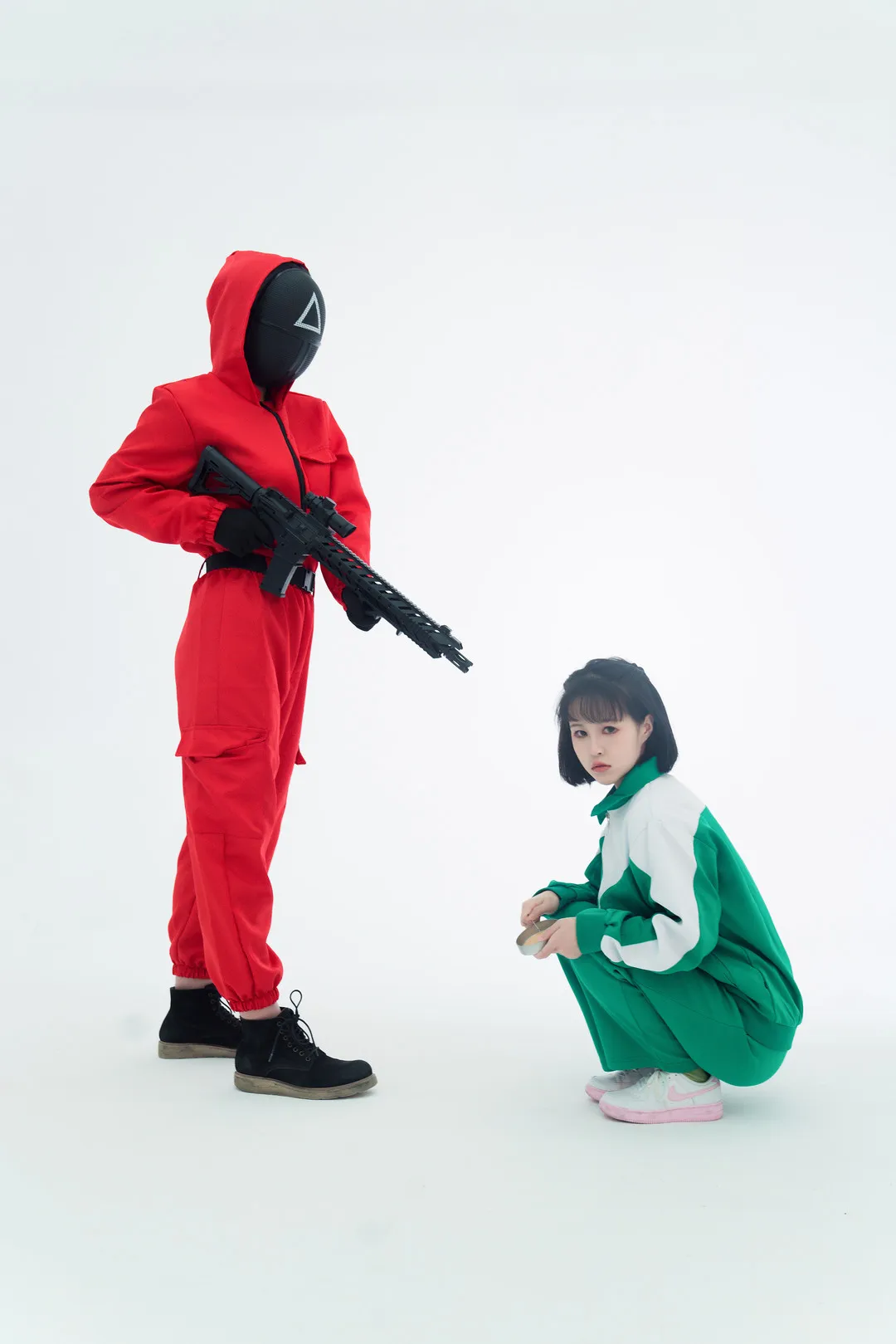 星澜是澜澜叫澜妹呀身穿绿色运动服蹲地，身旁站立着穿红衣戴面具持枪人员
