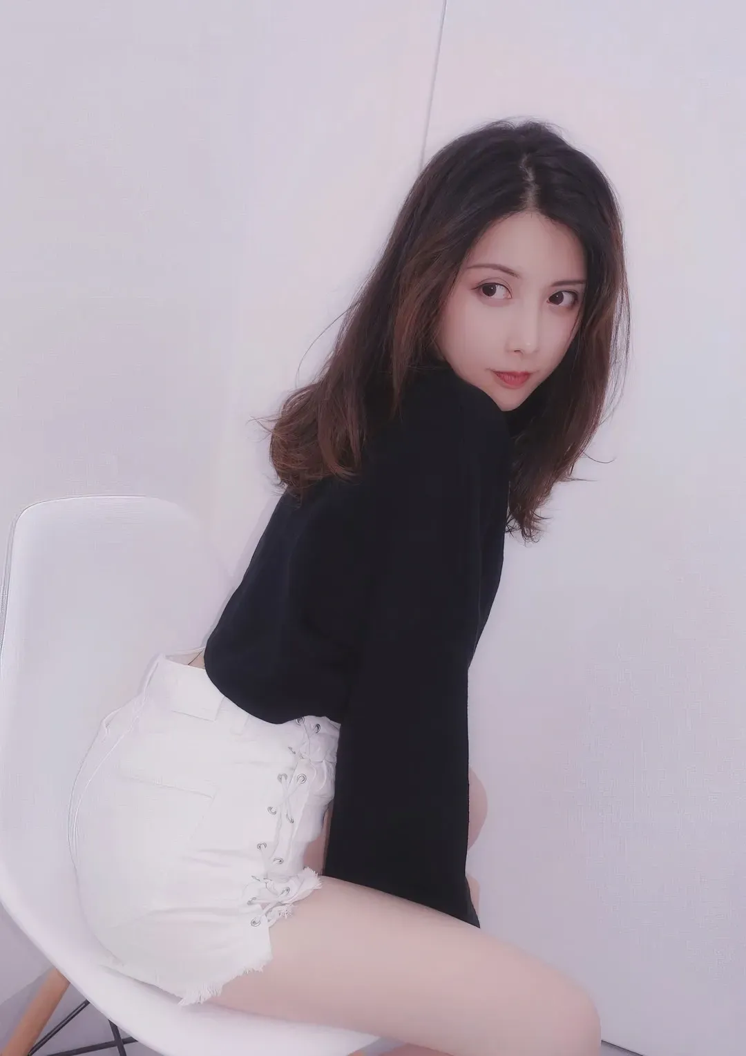 摄影师mix棚拍作品中身穿黑色高领针织衫与白色系带短裤坐在白椅上回眸凝视镜头的模特