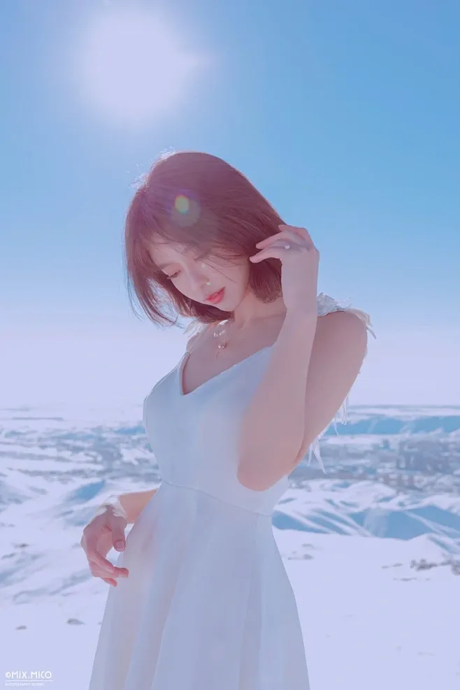摄影师mix雪山外景作品中身穿无袖白色深V连衣裙在强光雪景中轻抚发丝的模特