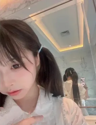 wink是可爱的wink扎双马尾佩戴发夹身穿白色蕾丝刺绣上衣在镜子前自拍